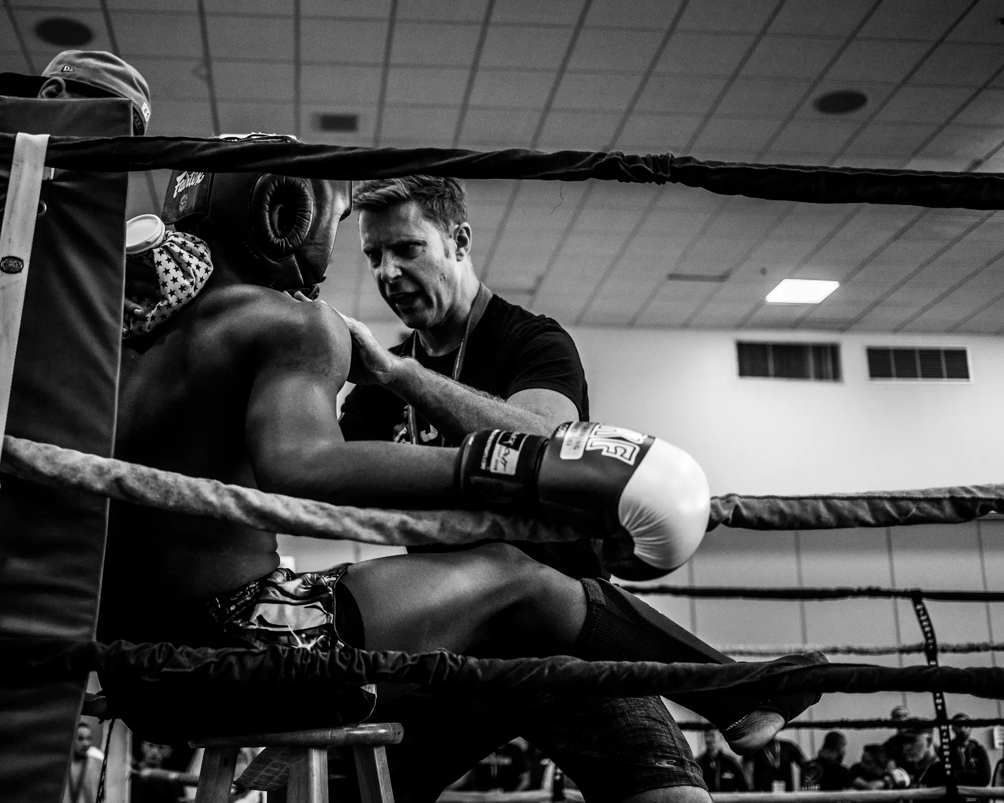 Entrenador corrigiendo la guardia de un boxeador entre asaltos, apoyado en las cuerdas del ring