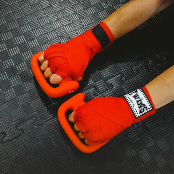 Manos vendadas con vendas de boxeo rojas sobre una colchoneta